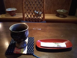 遊膳嵯溜沙(さるさ)の紙お手拭きとお茶の向こうに飾られている器と一緒に