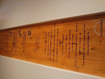 うどん三薫三沐の左の大きなテーブル向こうの壁に麺やダシについてのウンチクが書いてある