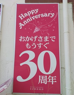SUMOMO志布志本店の横の駐車場側の壁に「もうすぐ30周年」とショッキングピンクに白文字の看板