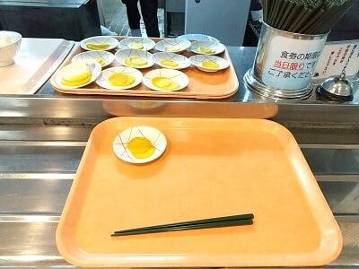 第一工大 学食(カフェテリア)のオレンジのトレイを受け取りカウンターに乗せてお箸とお漬物を乗せる