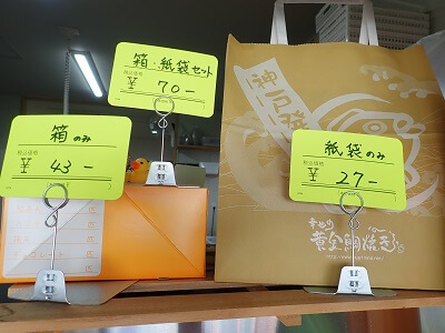 幸せの黄金鯛焼き・わらび屋本舗鹿児島店の実物大の紙袋や箱に料金が書いてある
